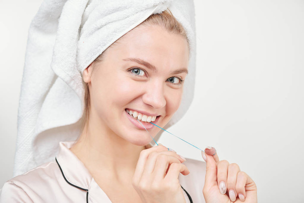 Χαρούμενη υγιής νεαρή γυναίκα με χαμόγελο toothy χρησιμοποιώντας οδοντικό νήμα μπροστά από την κάμερα στην απομόνωση - Φωτογραφία, εικόνα