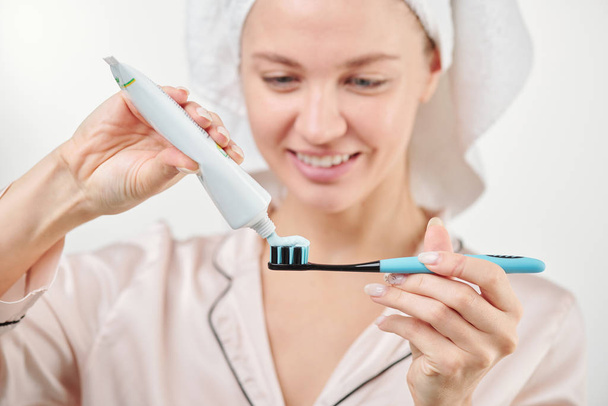 Main de la jeune femme en bonne santé appliquant du dentifrice sur la brosse à dents pendant les procédures d'hygiène matinale
 - Photo, image