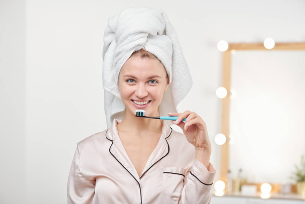 Jolie jeune femme tenant une brosse à dents par la bouche tout en regardant la caméra avec le sourire des dents
 - Photo, image