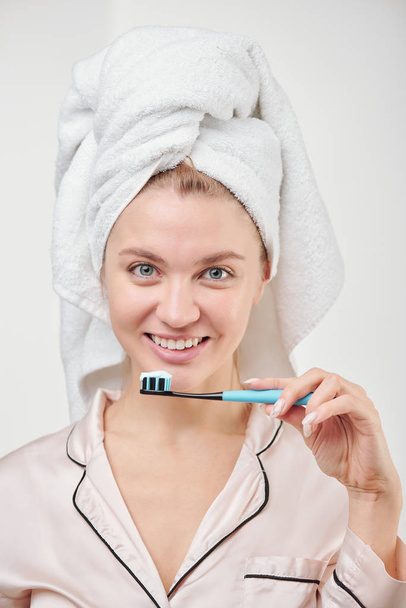 Όμορφη νεαρή υγιής γυναίκα με χαμόγελο toothy κρατώντας οδοντόβουρτσα, ενώ στέκεται μπροστά από την κάμερα στην απομόνωση - Φωτογραφία, εικόνα