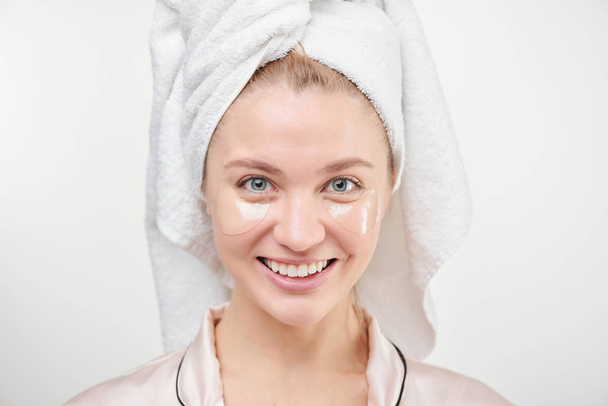 Healthy young woman with toothy smile enjoying refreshening under-eye procedure in isolation - Photo, Image