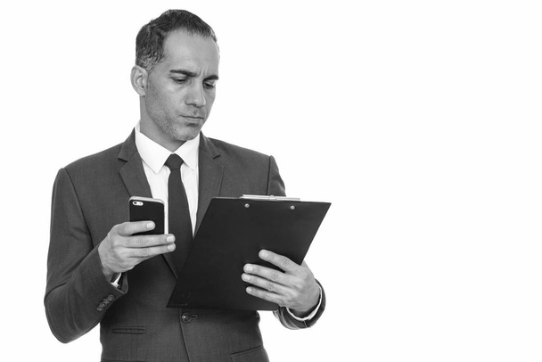 Mature handsome Persian businessman reading clipboard while holding mobile phone - Photo, Image