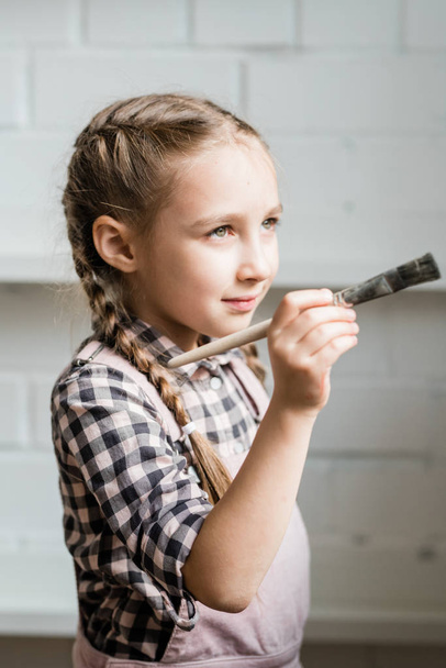 Creative and adorable schoolgirl holding paintbrush while going to paint picture in studio - Photo, Image