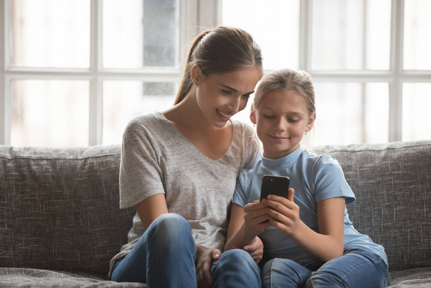 Sorrindo jovem mãe e filha usando celular em casa
 - Foto, Imagem