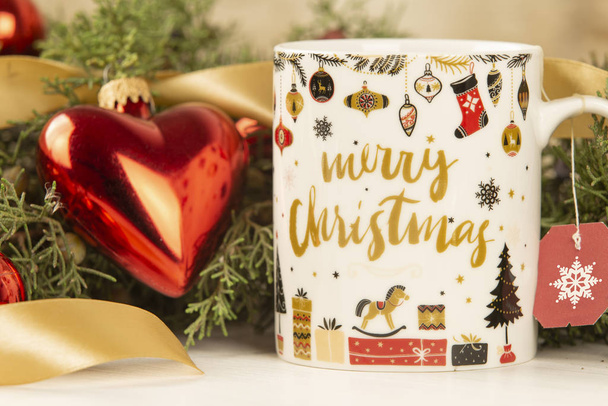 Primo piano di una tazza di Natale con etichetta da tè vuota appesa con intorno rami di pino, bagattelle rosse e nastro in oro satinato con effetto bokeh
 - Foto, immagini