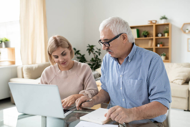 hübsche junge Frau mit Laptop und ihrem pensionierten Vater, der über häusliche Angelegenheiten berät oder zu Hause nach Daten sucht - Foto, Bild