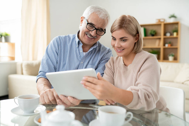 glücklicher alter Mann und seine kleine Tochter schauen auf den Touchpad-Bildschirm, während sie mit jemandem per Videochat sprechen - Foto, Bild