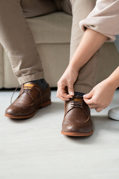Hands of careful young daughter helping her sick father sitting on couch to tie shoelaces on brown boots before going out - Foto, Imagen