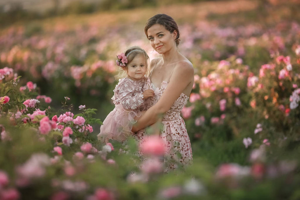 A woman in a retro dress with her daughter 5 years old walking in the spring in a field with roses - Photo, image