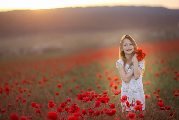 Red-haired girl 12-13 years old with flowers in her hair on the background of an agricultural field - Photo, Image