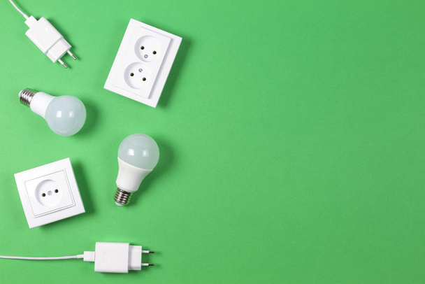 White electrical power sockets, power plugs, light lamp bulbs on light green background. Top view - 写真・画像