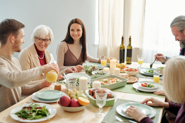 Jovem derramando suco de laranja para sua avó durante o jantar de família por mesa festiva servida no dia de Ação de Graças
 - Foto, Imagem