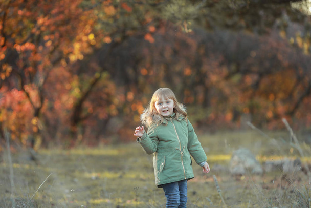 Iloinen lapsi kävelee syksyllä puutarhassa, jossa puut peitetään keltaisella lehdellä.
 - Valokuva, kuva