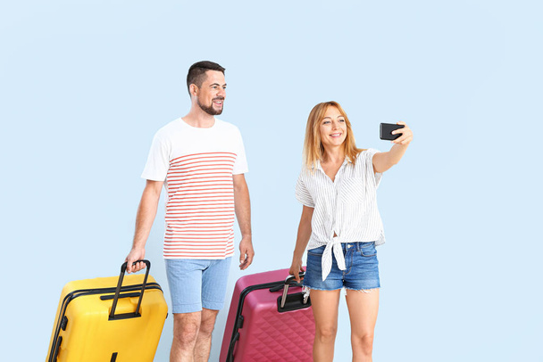 Couple with suitcases taking selfie on color background - Fotografie, Obrázek