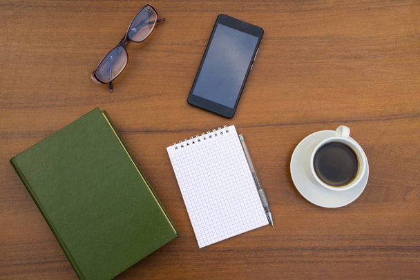 Чашка кофе, книга, блокнот, ручка, очки и смартфон на деревянном столе
 - Фото, изображение