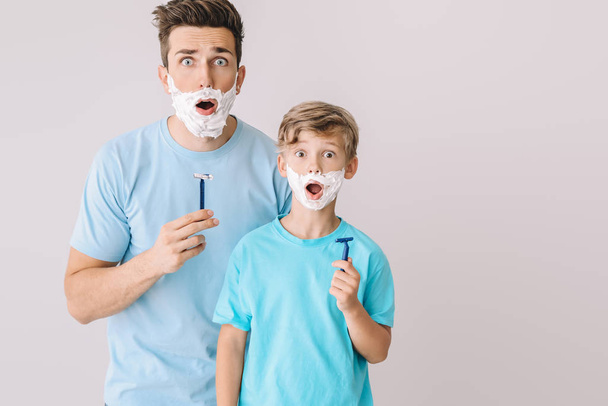 Grappige vader en zijn kleine zoon scheren tegen grijze achtergrond - Foto, afbeelding