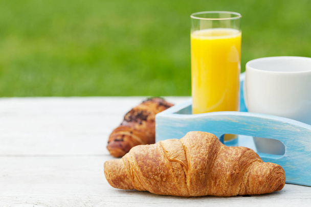 Koffie, sinaasappelsap en croissant op zonnige tuintafel. Frans ontbijt. Met kopieerruimte voor uw tekst - Foto, afbeelding