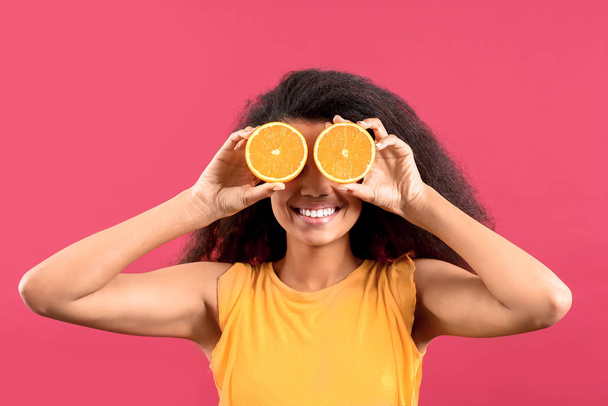 Happy African-American woman with orange fruit pieces on color background - Photo, Image