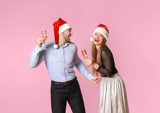 Ευτυχισμένο ζευγάρι σε καπέλα Άγιος Βασίλης και με ποτήρια σαμπάνιας στο φόντο χρώμα - Φωτογραφία, εικόνα