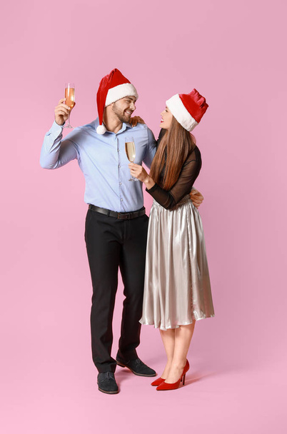 Noel Baba şapkalı mutlu çift ve renkli arka planda şampanya kadehleri - Fotoğraf, Görsel