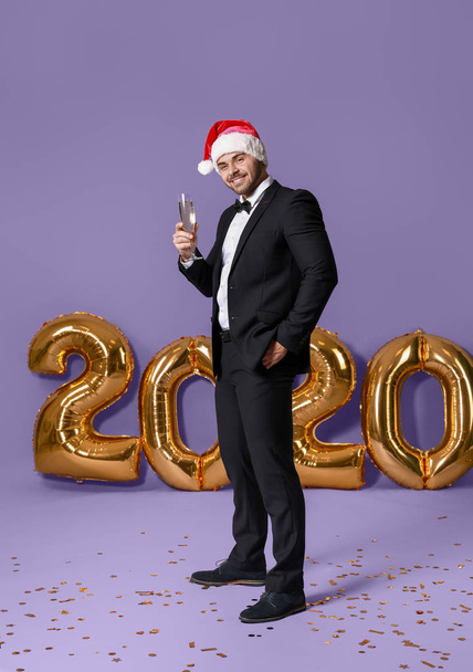 Knappe jongeman in Santa Claus hoed en met glas champagne op kleur achtergrond - Foto, afbeelding