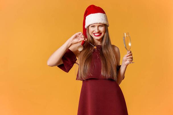 Šťastná mladá žena v klobouku Santa Claus, s vánoční jiskru a sklenice šampaňského na barevném pozadí - Fotografie, Obrázek