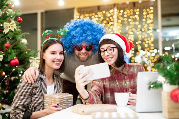 Groupe de jeunes collègues heureux en tenue traditionnelle de Noël faire selfie par lieu de travail au bureau le jour de Noël
 - Photo, image