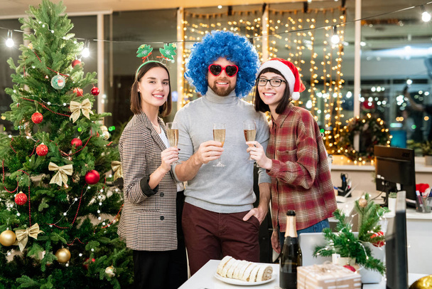 Group of happy young businesspeople toasting for Christmas with flutes of champagne while enjoying party in office - 写真・画像
