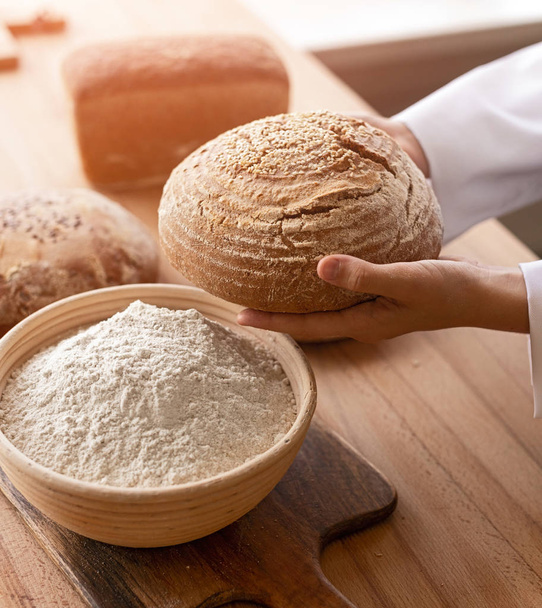 Crop baker carrying bread near flour - 写真・画像