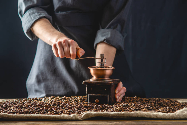 Hände Baristas in einer dunklen Schürze mahlen an einer Handmühle duftenden Kaffeebohnen. Auswahl an frischem Kaffee für Espresso - Foto, Bild