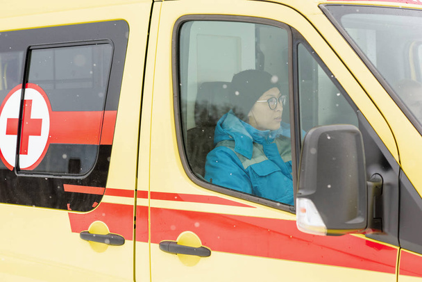 Молода жінка-парамедик у формі та кепці сидить у машині швидкої допомоги, поспішаючи допомогти та врятувати хворого
 - Фото, зображення