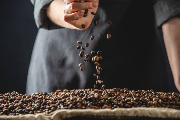 Mão derramando grãos de café perfumados em uma pilha de grãos de arábica assada. Seleção de café fresco para café expresso - Foto, Imagem