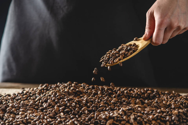Las manos vierten granos de café fragantes en una ráfaga. Pile de cereales arábicos tostados. Selección de café fresco para espresso - Foto, Imagen