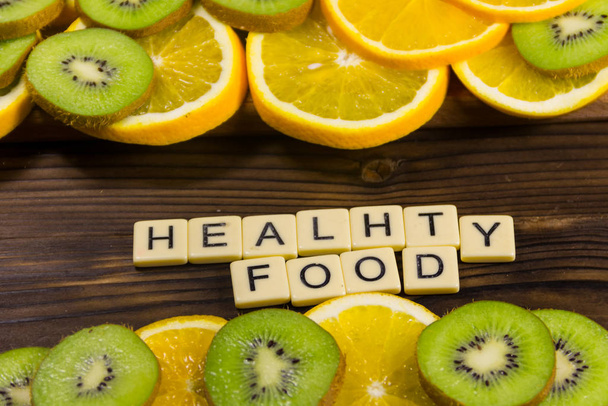 Kiwi en rodajas y naranjas con inscripción "comida saludable" en la mesa de madera. Concepto de dieta. Vista superior
 - Foto, imagen