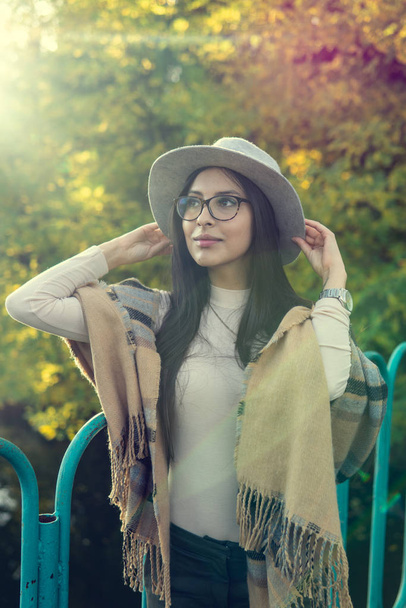 Close up of happy emotionally brunette woman with long hair and glasses in hat. Beautiful model with perfect makeup after salon, posing in park. Concept of fashion and beauty. - Photo, image