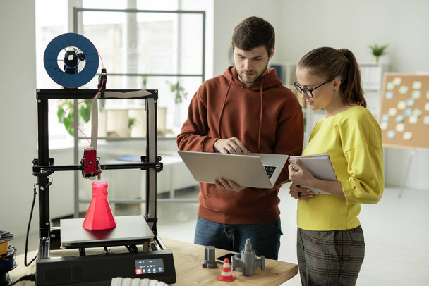 zwei junge kreative Designer auf der Suche nach neuen Online-Ideen für kreative Projekte, während sie vor dem 3D-Drucker stehen - Foto, Bild