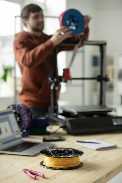 Spule mit gelbem Filament und Zangen am Arbeitsplatz des kreativen Designers, der neue Fäden in 3D-Drucker einbindet - Foto, Bild