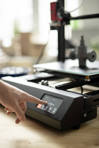 Ruka mladého designéra stiskem tlačítka start na ovládacím panelu 3D tiskárny před zahájením pracovního procesu - Fotografie, Obrázek
