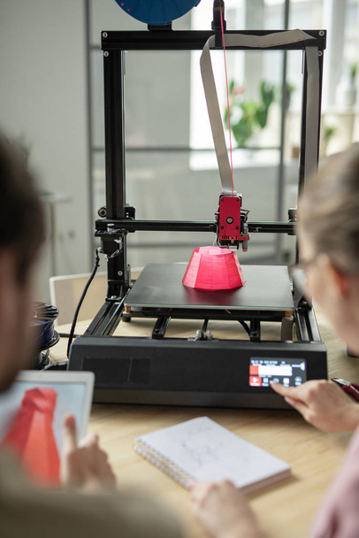 Roze ronde 3D-object wordt afgedrukt terwijl jonge vrouw aanraken knop op het bedieningspaneel van de printer - Foto, afbeelding