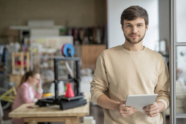 Молодой привлекательный бизнесмен с планшетным серфингом в сети для творческих сайтов на фоне коллеги по 3D принтер
 - Фото, изображение