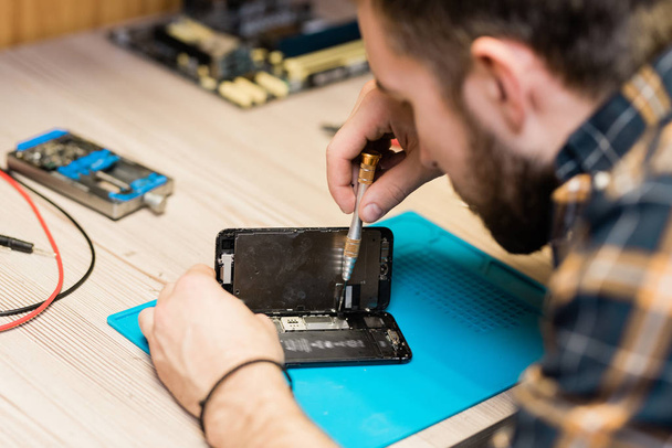 Professional gadget repair service master holding cover of smartphone while fixing tiny details with special screwdriver - Foto, Imagen