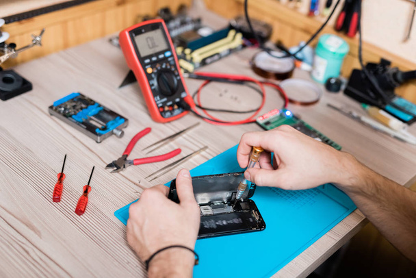Hands of gadget repair service master using screwdriver while fixing tiny details of demounted smartphone - Foto, Imagem