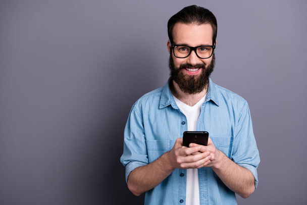 Portrait of positive cheerful freelancer guy blogger use cellphone read social media information wear stylish jeans denim clothing isolated over grey color background - Photo, Image