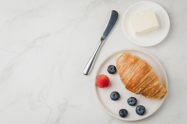 Croissant with berries in white bowl and butter knife on white s - Photo, image