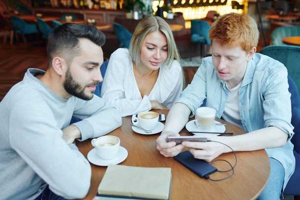Група випадкових друзів коледжу, які сидять за столом у кафе після занять, мають каву і дивляться цікаві речі в смартфоні
 - Фото, зображення