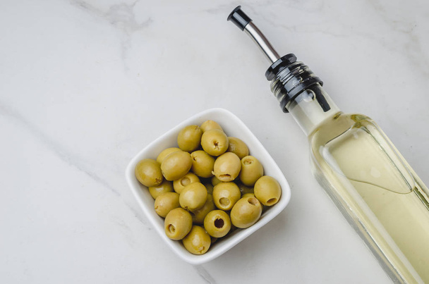 Green olives in a white ceramic bowl and glass bottle of olive o - Foto, immagini