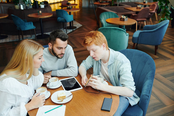 Casual guy avec smartphone montrant des choses en ligne à ses amis tout en en discutant par table dans un café après les cours
 - Photo, image