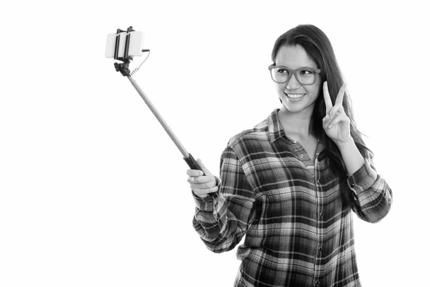 Joven mujer feliz sonriendo mientras toma foto selfie con palo de selfie y dando señal de paz
 - Foto, Imagen