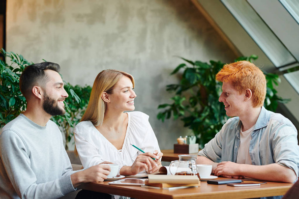 Група щасливих молодих друзів сучасного коледжу зібралися за столом у кафе після занять для обговорення домашнього завдання
 - Фото, зображення
