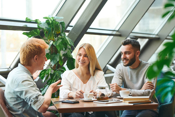 コーヒーや紅茶を飲みながらおしゃべりをしたり、クラスの後にカフェでテーブルに集まった幸せな若い現代の学生のグループ - 写真・画像